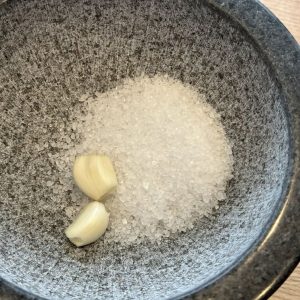 Knoblauch und grobes Salz im Granitmörser – Vorbereitung für selbstgemachtes Knoblauchsalz