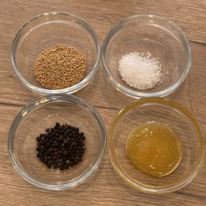 Honig Senf Rub Zutaten im Überblick – Senfkörner, grobes Salz, schwarzer Pfeffer und Honig für BBQ Rub aus dem Mörser