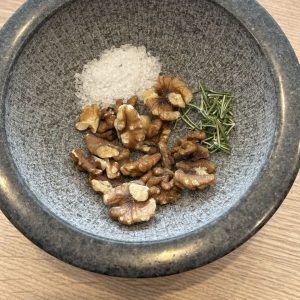 Walnüsse, Salz und Rosmarin im Mörser – Zubereitung eines Nuss Kräuter Toppings für Grillgerichte