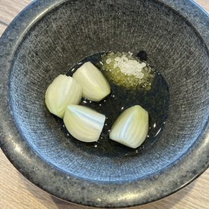 Zwiebel Gewürzpaste im Mörser – Zwiebelstücke mit Salz und Olivenöl vor dem Zerdrücken