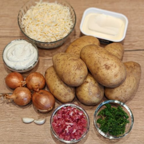 Zutaten für Grillkartoffeln mit Käse, Kräuterbutter, Zwiebeln, Schinkenwürfeln und Sour Cream auf Holzbrett