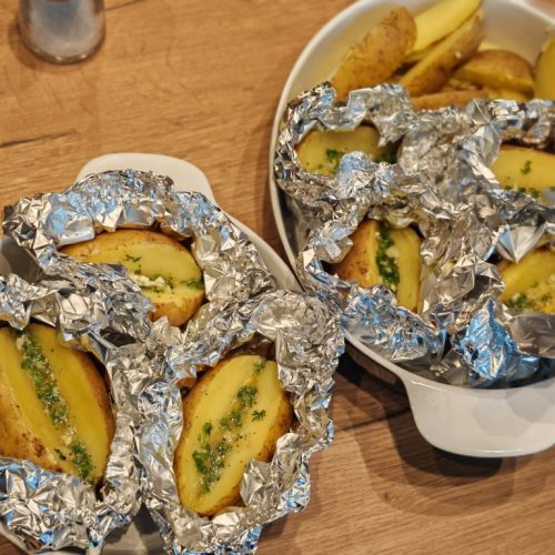 Mehrere mit Kräuterbutter gefüllte Kartoffeln in Alufolie vor dem Grillen