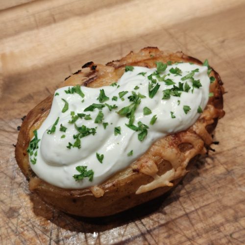 Fertige gefüllte Grillkartoffel mit Sour Cream und Petersilie auf Holzbrett