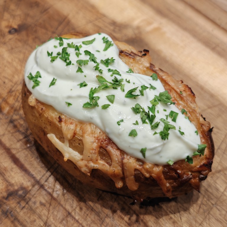 Nahaufnahme einer gefüllten Grillkartoffel mit Käse, Sour Cream und Petersilie