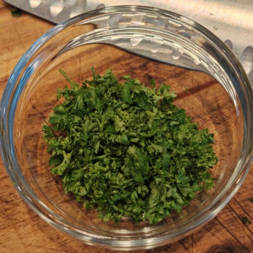 Frisch gehackte Petersilie in einer Glasschüssel auf einem Holzbrett