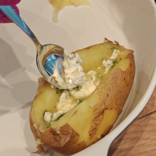 Kräuterbutter wird mit einem Löffel in eine aufgeschnittene Kartoffel gefüllt